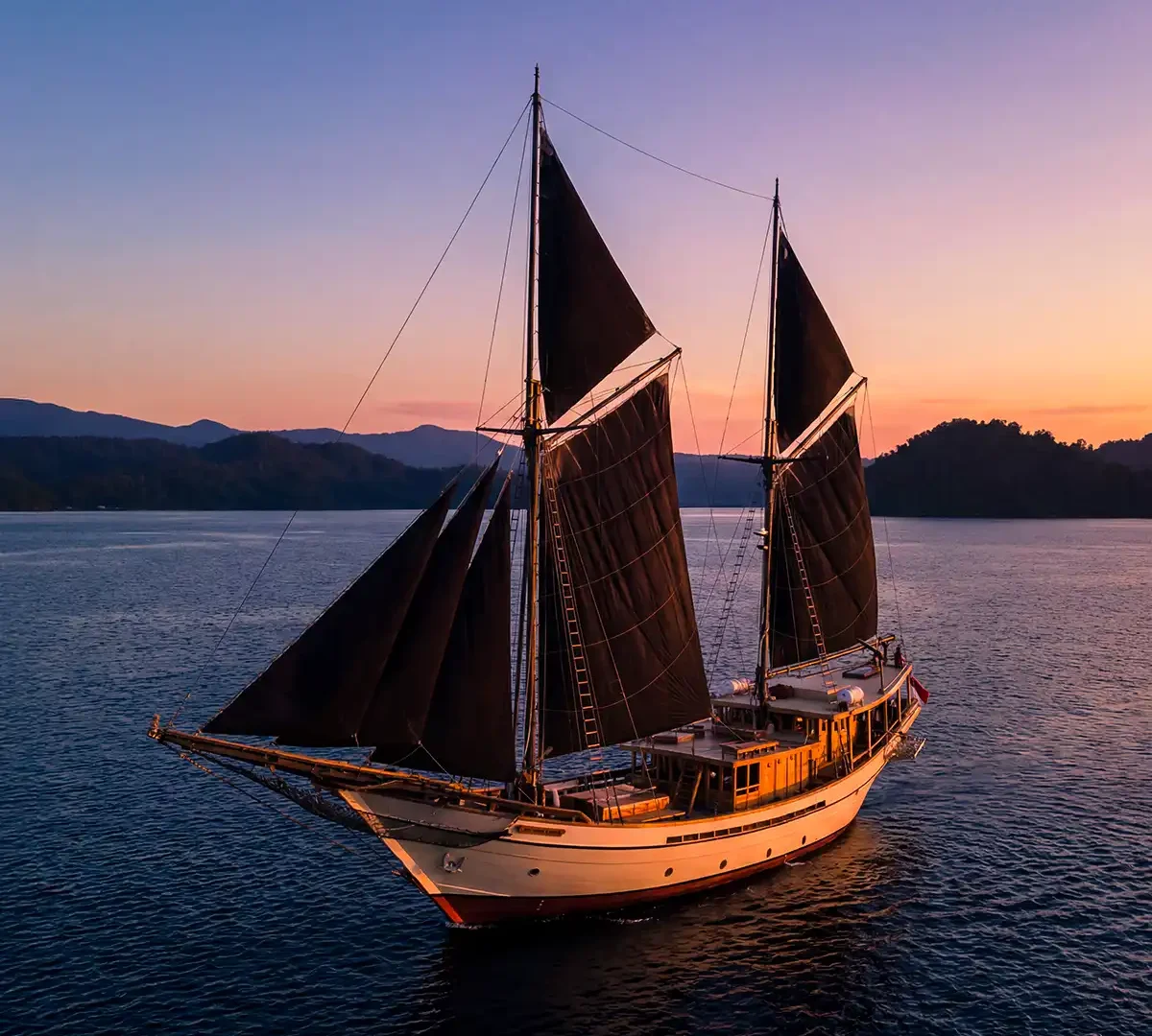 Phinisi with dark sails sailing at dusk