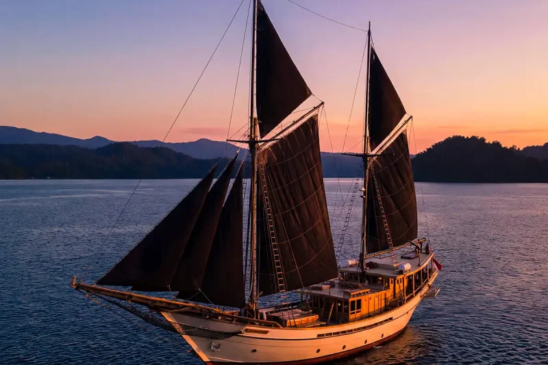Phinisi with dark sails sailing at dusk