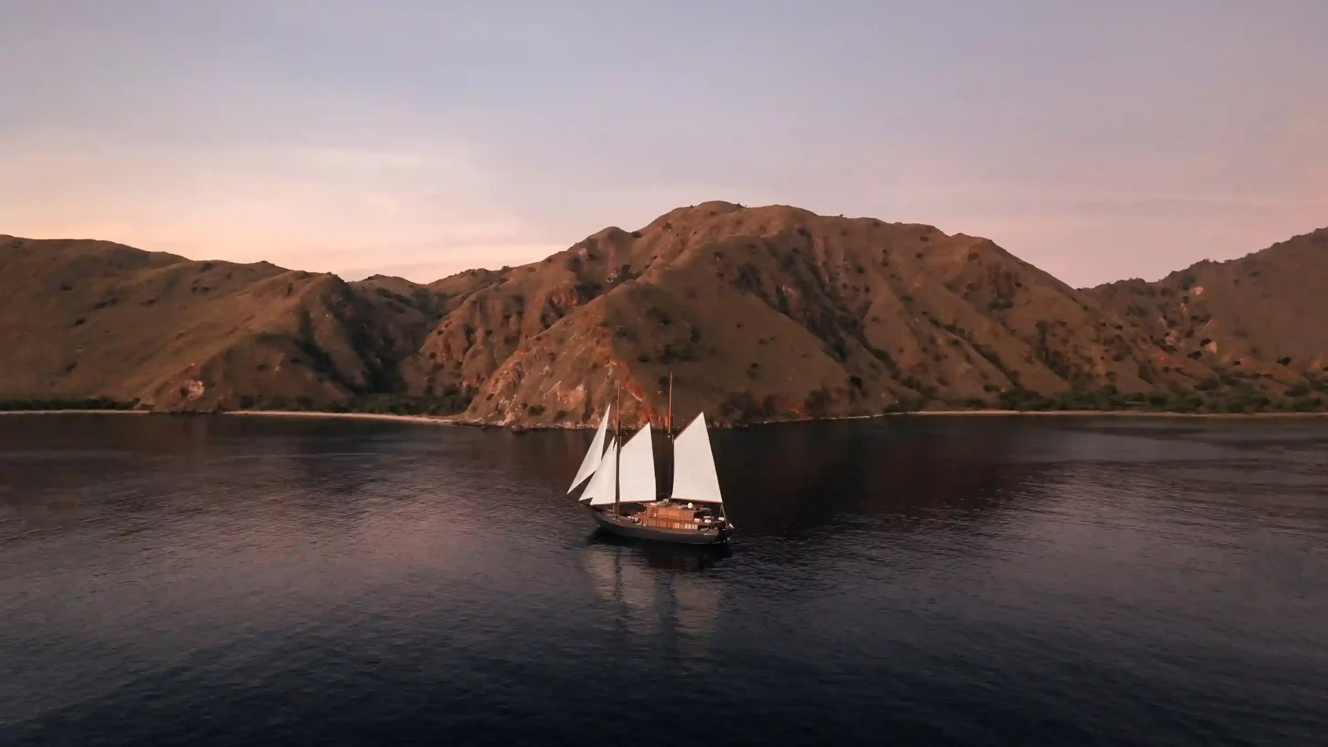 White-sailed phinisi gliding past Komodo hills